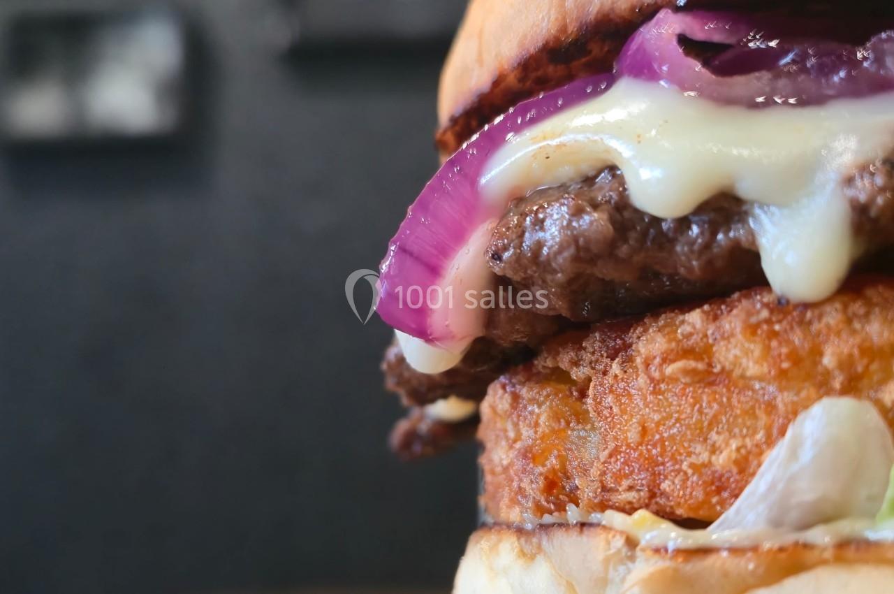 Gros plan d'un burger avec steak, fromage fondu, rondelle d'oignon rouge et galette croustillante.