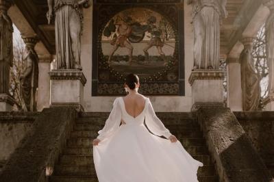 Un couple monte des marches, la mariée en robe blanche et voile, entourée d'invités élégamment vêtus.