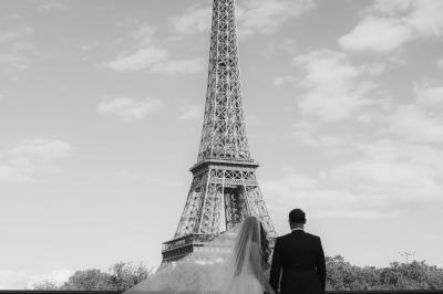 Un couple monte des marches, la mariée en robe blanche et voile, entourée d'invités élégamment vêtus.