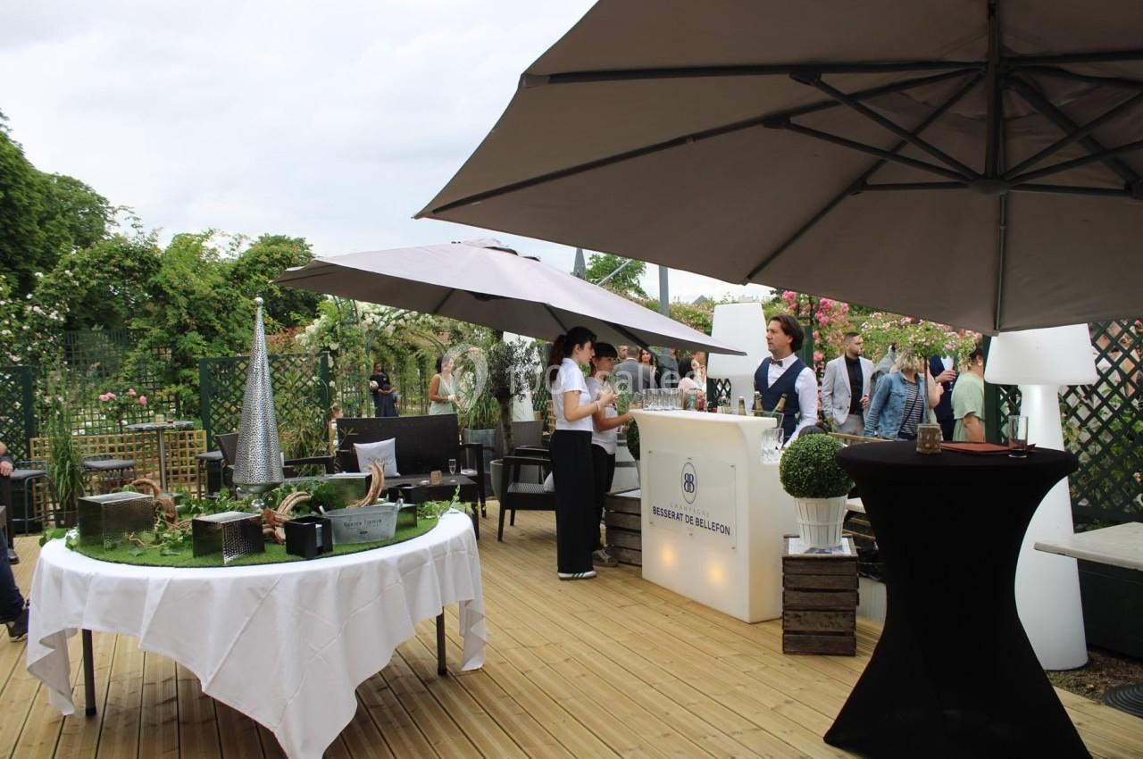 Un espace extérieur avec terrasse en bois, tables décorées, parasols et un comptoir de service animé par du personnel.