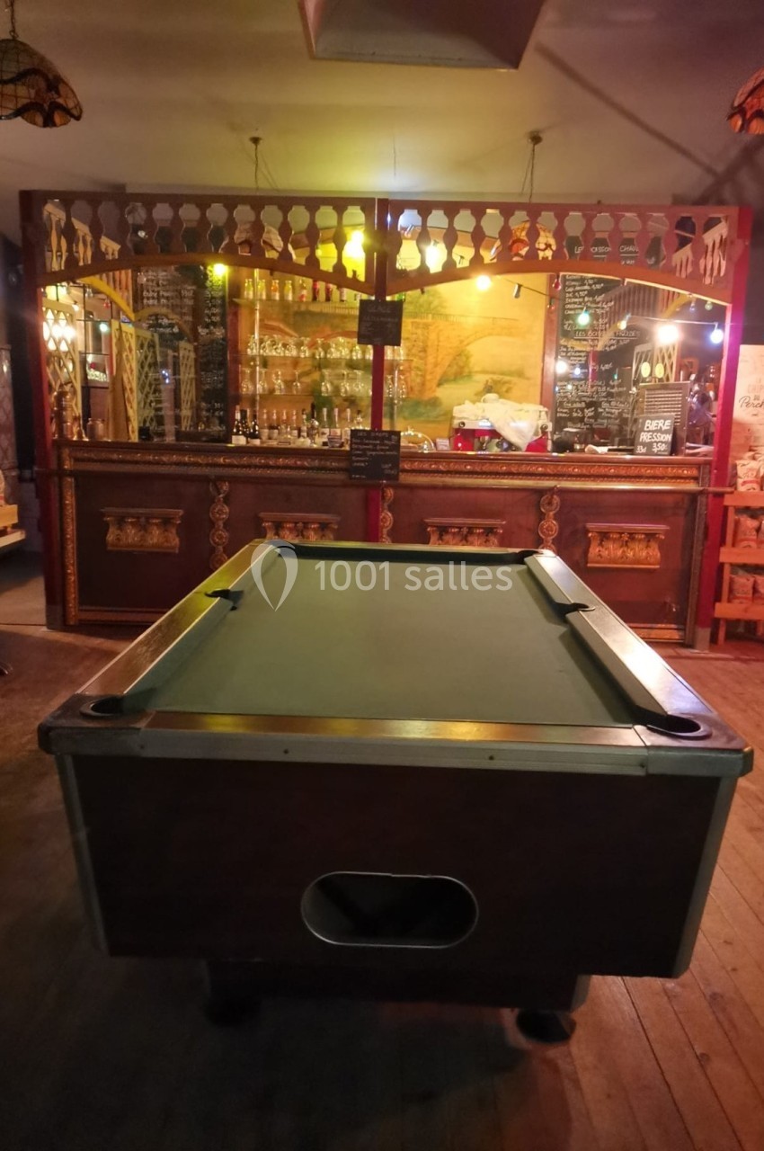 Table de billard vide dans un bar à l'ambiance chaleureuse, avec un comptoir en bois en arrière-plan.