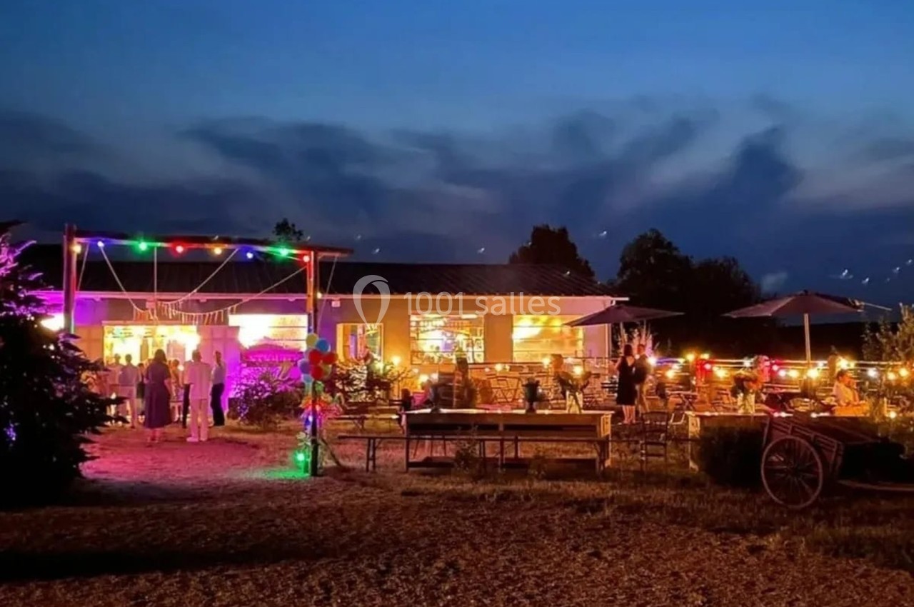 Extérieur d'un restaurant illuminé avec des guirlandes colorées, des tables en terrasse et un ciel nocturne dégagé.