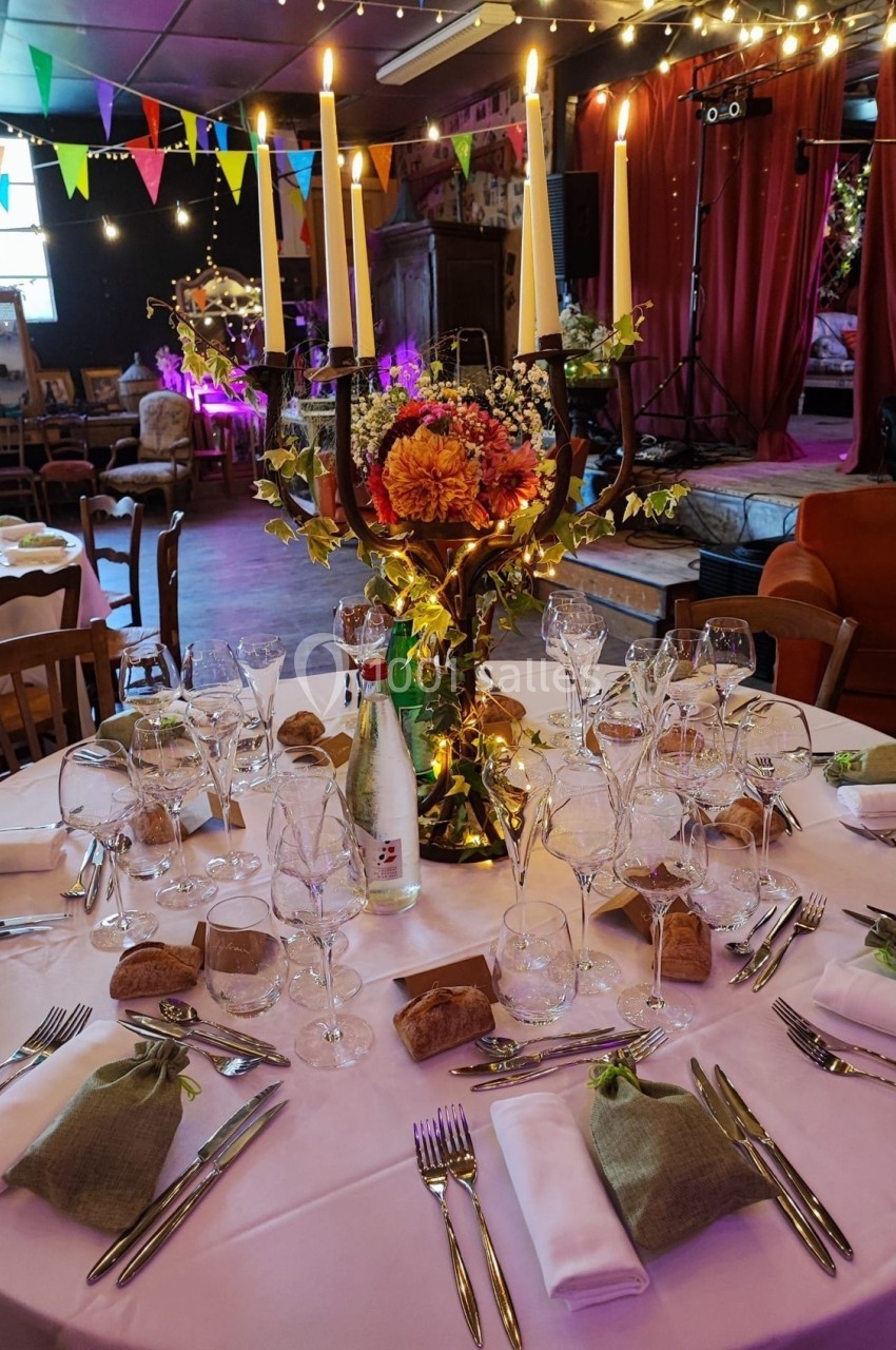 Table décorée pour un dîner festif avec chandeliers, fleurs, verres, couverts et pain, dans une salle ornée de guirlandes.