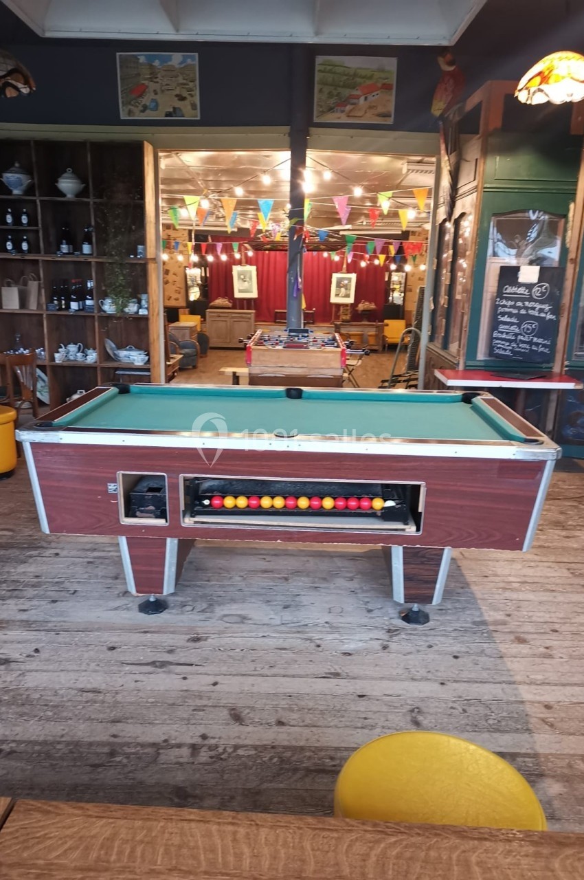 Table de billard rouge avec des boules alignées, située dans un espace intérieur décoré de guirlandes colorées.