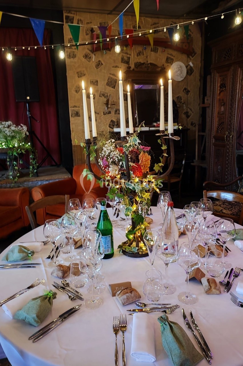 Table ronde décorée pour un dîner, avec chandelier, fleurs, verres et couverts, dans une salle festive et chaleureuse.