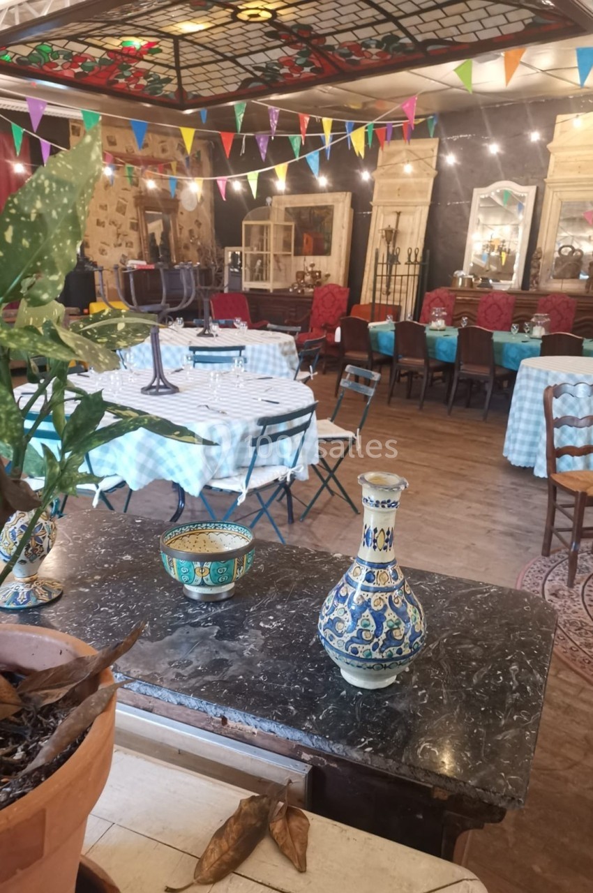 Salle décorée de façon vintage avec tables dressées, nappes à carreaux, plantes et guirlandes colorées suspendues.