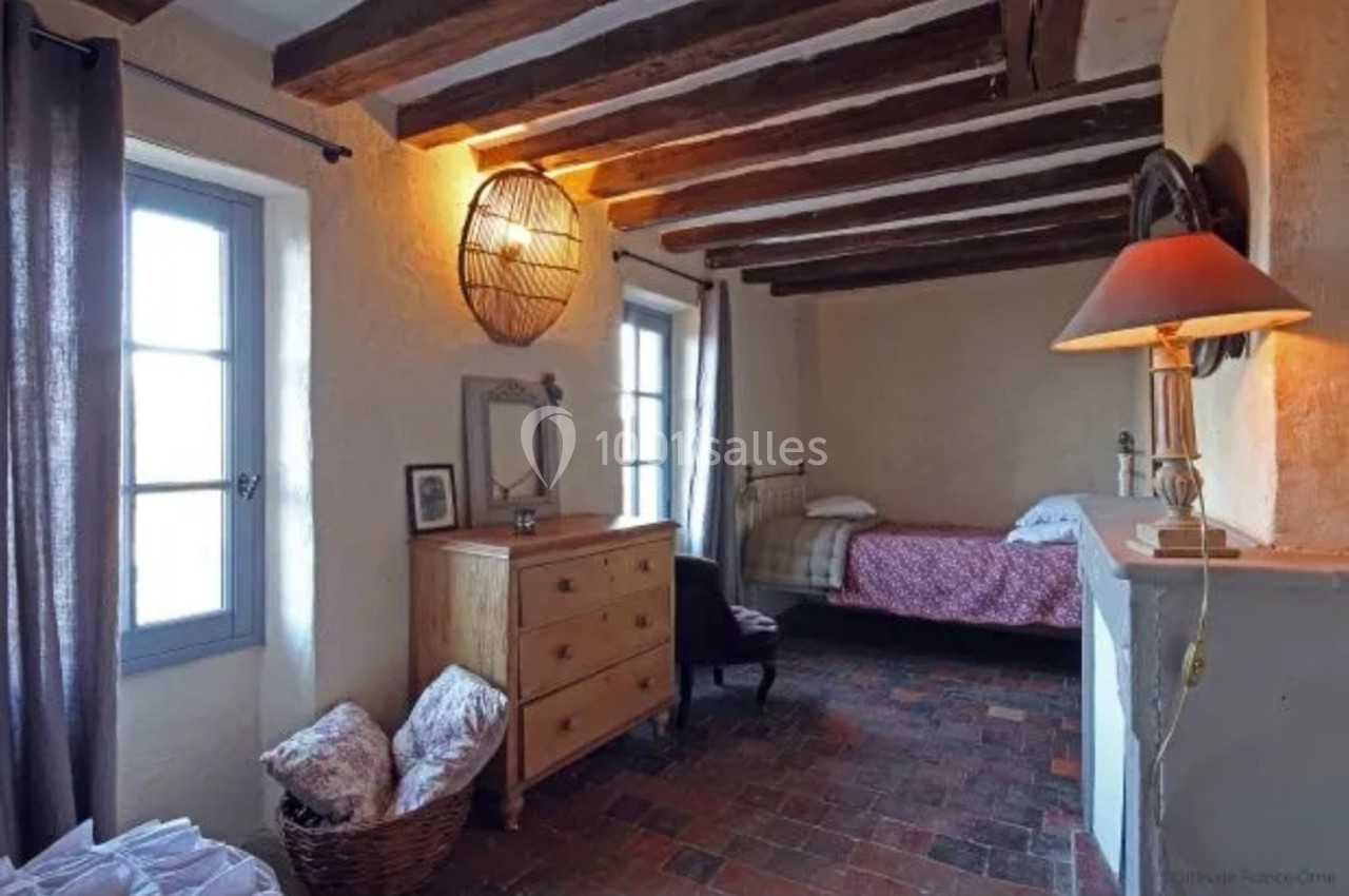 Chambre rustique avec poutres apparentes, lit simple, commode en bois, panier d'osier et lumière tamisée.