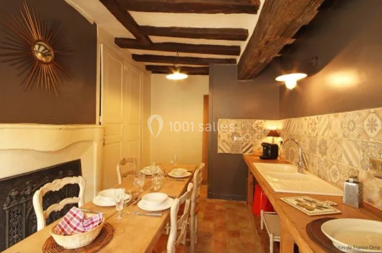 Cuisine rustique avec poutres apparentes, table en bois dressée pour quatre personnes et évier en céramique.