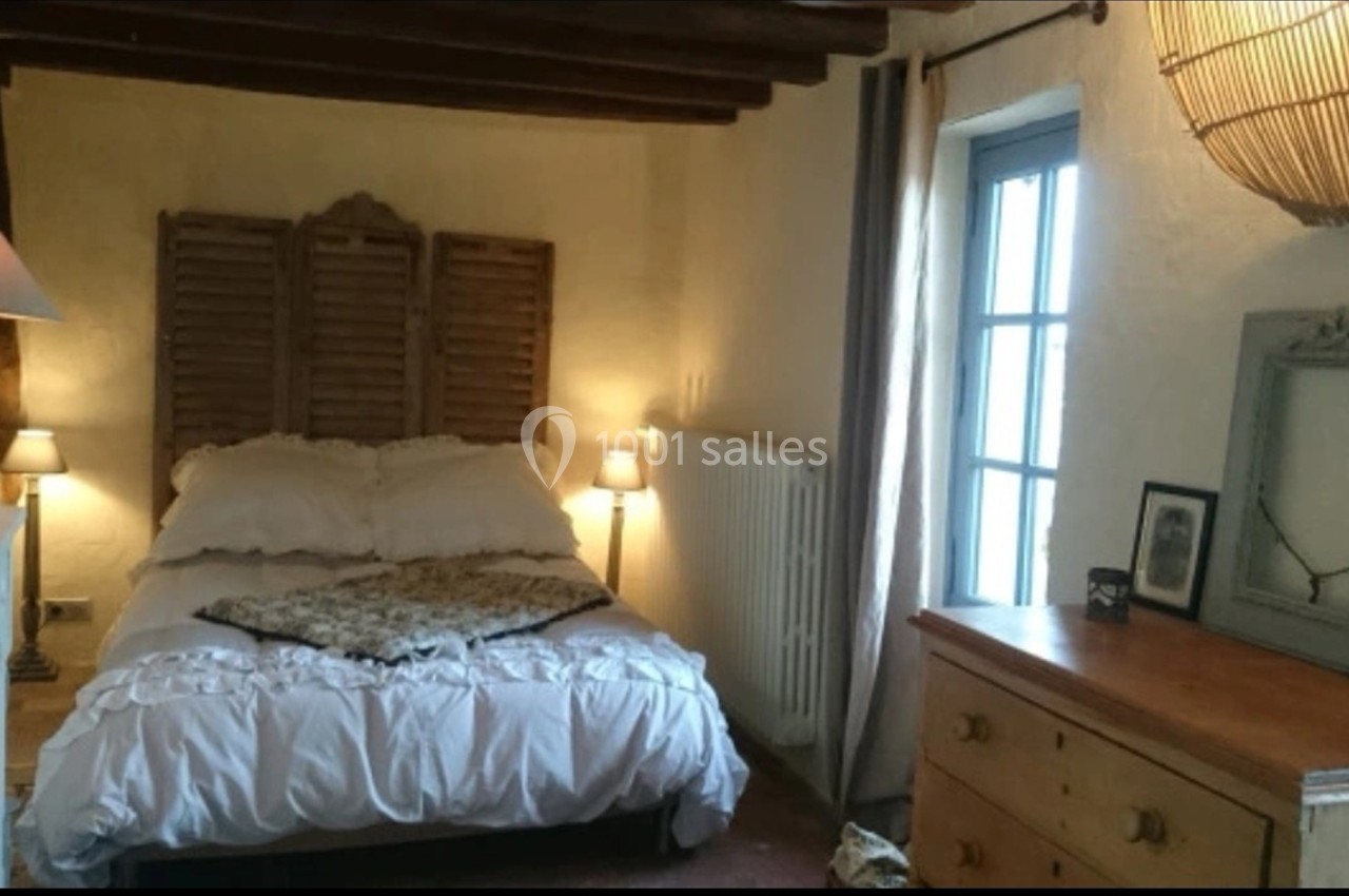 Chambre rustique avec lit double, murs clairs, poutres apparentes, commode en bois et fenêtre laissant entrer la lumière.