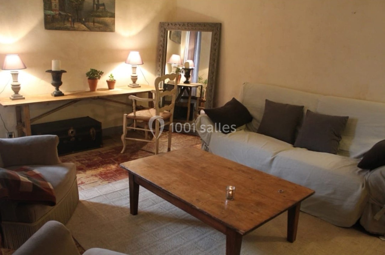 Salon chaleureux avec canapé, fauteuils, table basse en bois, bureau d'angle, miroir et éclairage doux.