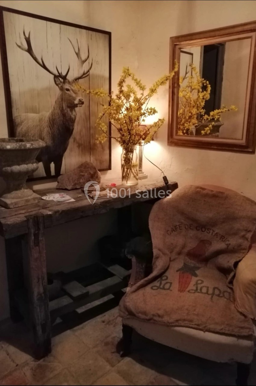 Intérieur rustique avec une table en bois, un fauteuil recouvert de toile de jute, des fleurs jaunes et un tableau de cerf.
