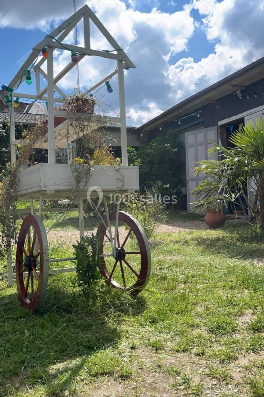 Chariot en bois blanc avec des plantes, posé sur une pelouse dans une cour ensoleillée entourée de bâtiments.