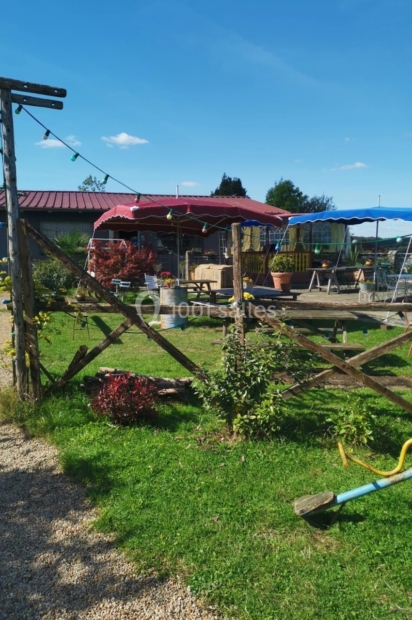 Espace extérieur avec tables, chaises, plantes et structures en bois sous un ciel bleu.