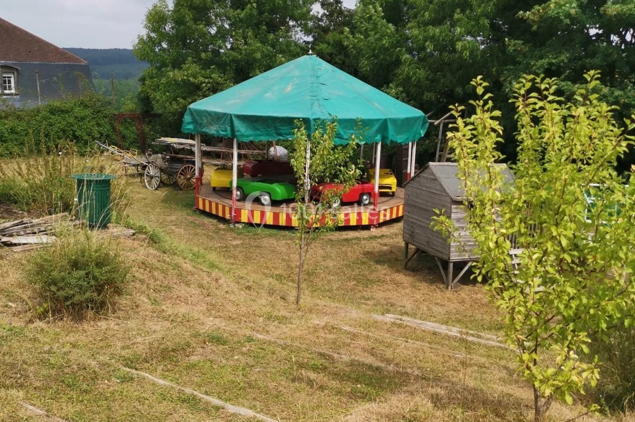 Manège pour enfants avec voitures miniatures sous un chapiteau vert, installé dans un jardin herbeux.