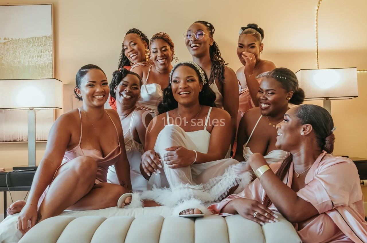 Un groupe de femmes souriantes, certaines en robes roses, assises sur un lit dans une ambiance chaleureuse.