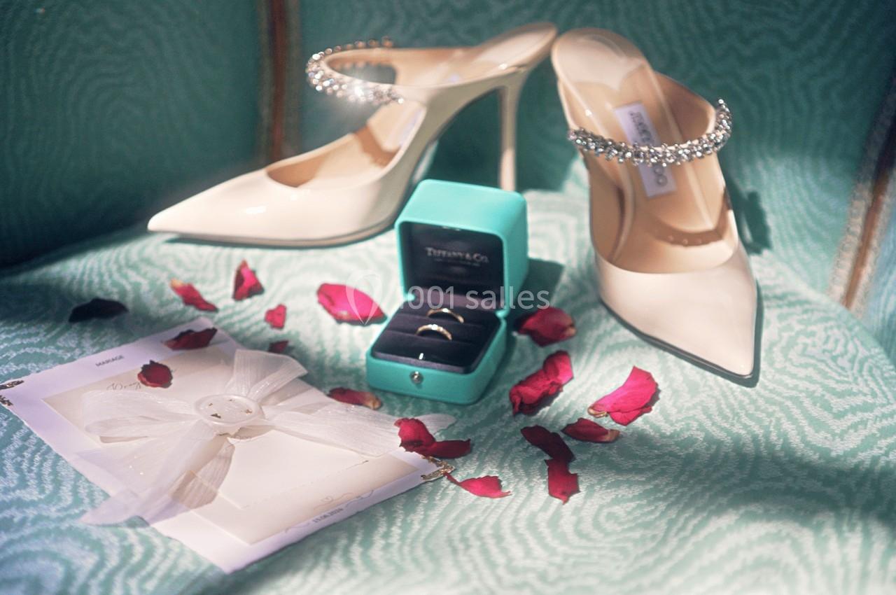 Chaussures à talons, boîte à bijoux ouverte avec bagues, pétales de rose et enveloppe sur un fauteuil vert.