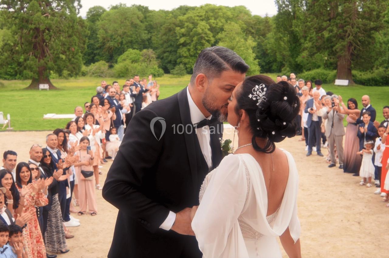 Un couple de mariés s'embrasse devant leurs invités rassemblés en plein air dans un cadre verdoyant.