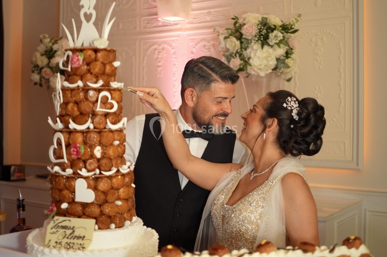 Un couple souriant partage un moment devant une pièce montée décorée de cœurs lors d'une réception.