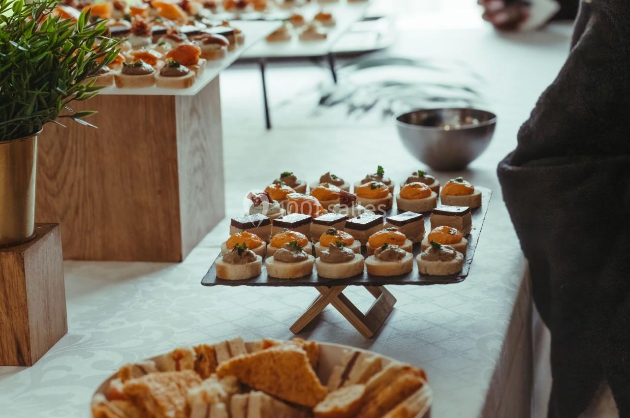 Plateau de canapés variés disposés sur une table lors d'un buffet, avec des plantes et des plats en arrière-plan.