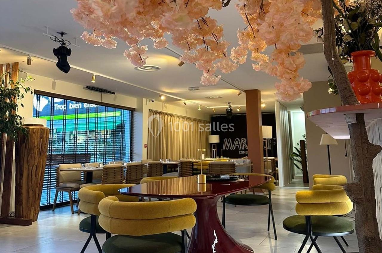 Salle de restaurant moderne avec des chaises jaunes, une table rouge et une décoration florale suspendue.