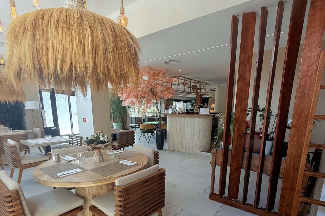 Salle de restaurant lumineuse avec mobilier en bois, décoration végétale et comptoir en arrière-plan.