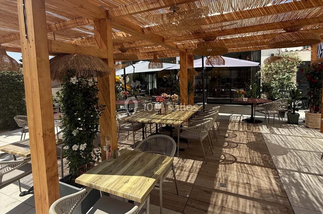 Terrasse en bois ombragée avec tables, chaises et plantes, entourée de parasols et d'une végétation décorative.