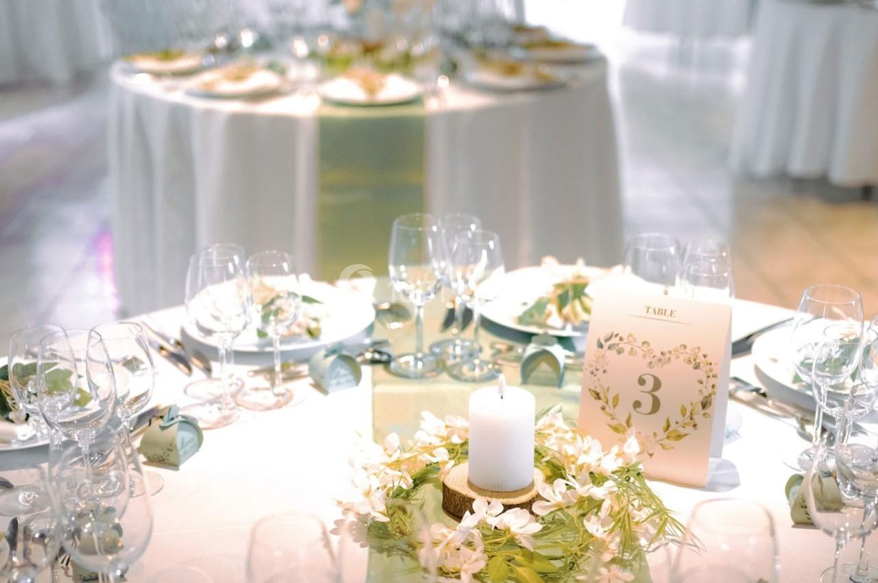 Table décorée pour un événement avec bougie centrale, fleurs blanches et numéro de table inscrit sur un carton.