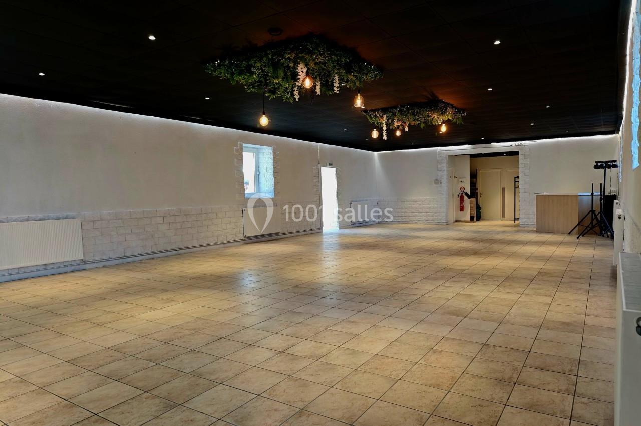 Salle spacieuse avec carrelage clair, murs blancs, plafond noir décoré de végétation et éclairage suspendu.