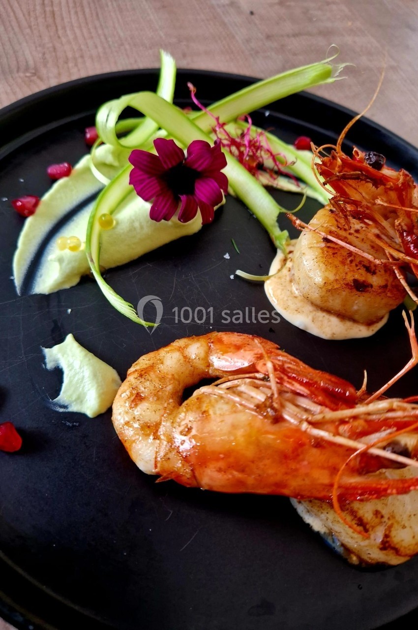 Assiette gastronomique avec crevettes grillées, noix de Saint-Jacques, purée verte, rubans de légumes et fleur comestible.