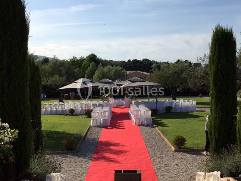 Allée rouge menant à une cérémonie en plein air, entourée de chaises blanches et de jardins verdoyants.
