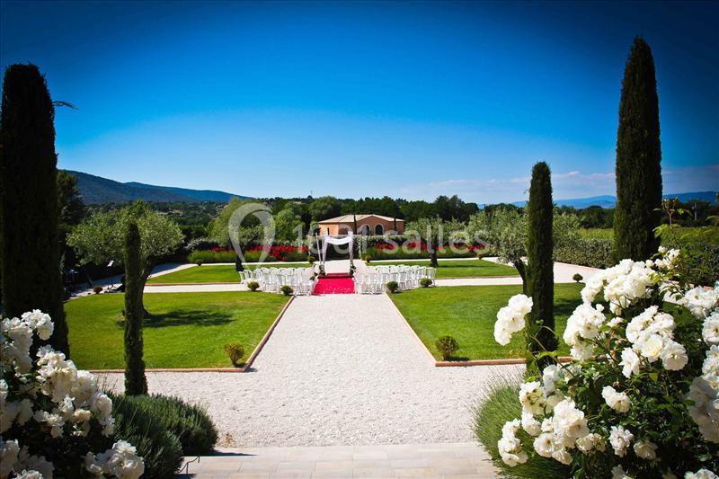 Allée bordée de cyprès menant à une cérémonie en plein air avec chaises blanches et arche, entourée de jardins verdoyants.