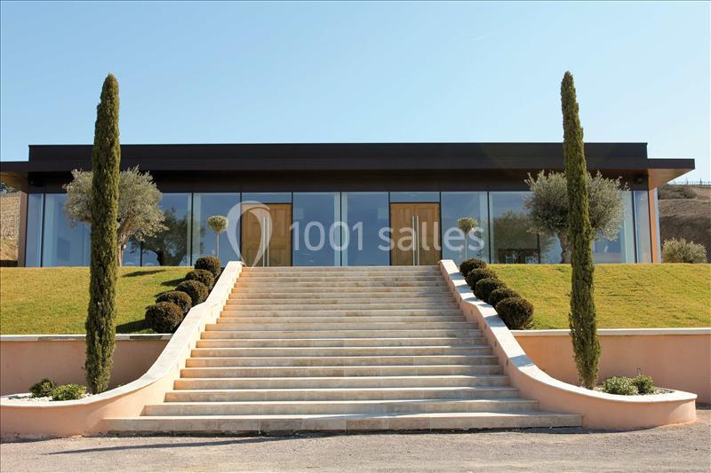 Escalier en pierre menant à un bâtiment moderne avec façade vitrée, entouré de pelouse et d'arbres taillés.