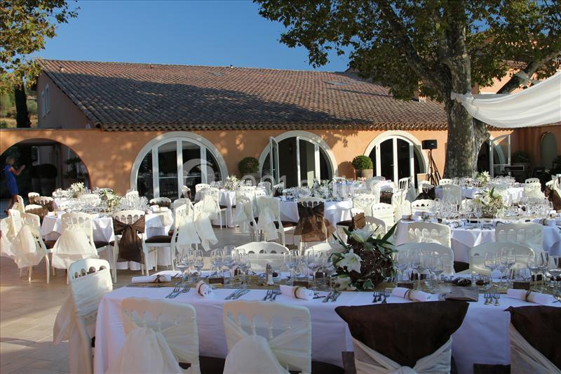 Tables élégamment dressées pour un événement en plein air devant un bâtiment à arcades et toit en tuiles.