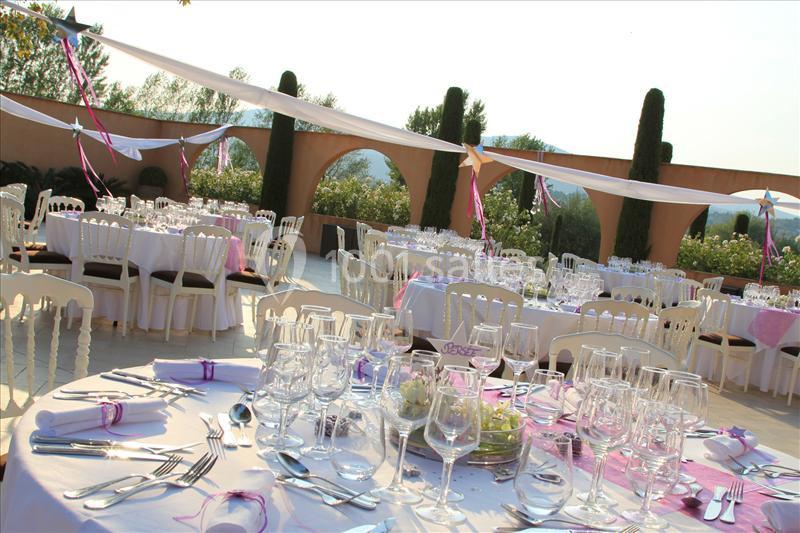 Tables élégamment dressées pour un événement en plein air, avec nappes blanches, rubans roses et décorations florales.