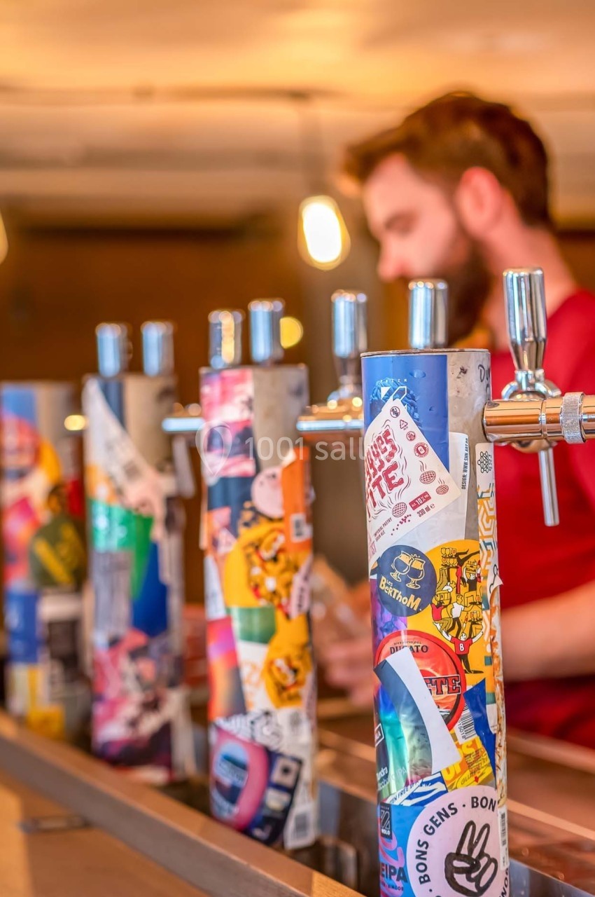 Robinets de bière décorés d'autocollants colorés dans un bar, avec un barman flou en arrière-plan.