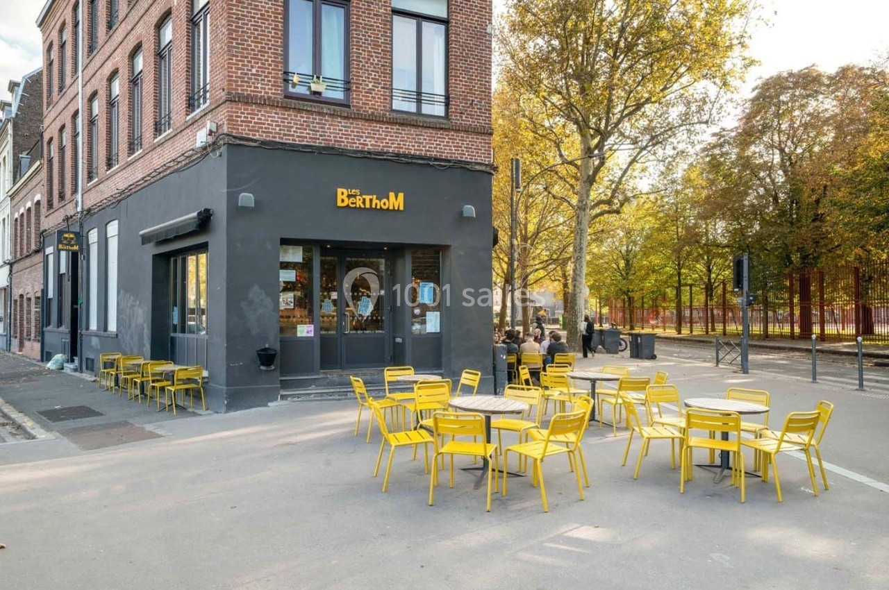 Façade d'un restaurant avec terrasse extérieure équipée de tables et chaises jaunes, situé près d'un parc arboré.