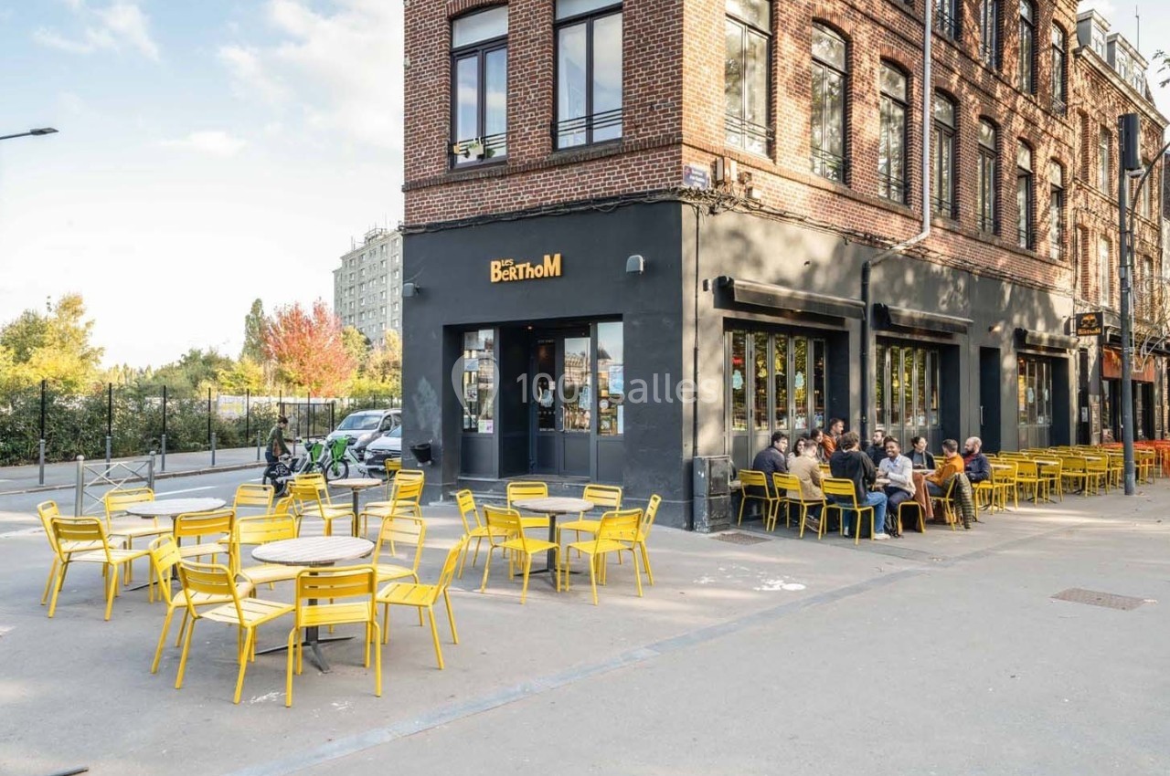 Façade d'un café-restaurant en briques avec terrasse extérieure équipée de chaises et tables jaunes.