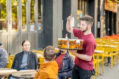 Un couteau et un saucisson sec posé sur une planche en bois, avec un verre de bière en arrière-plan.