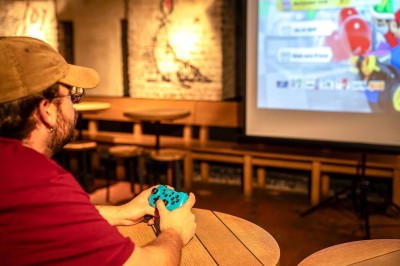 Un couteau et un saucisson sec posé sur une planche en bois, avec un verre de bière en arrière-plan.