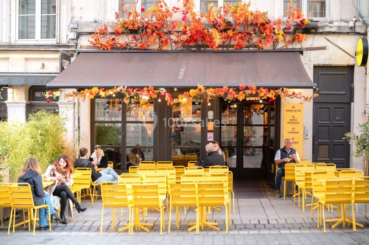 Terrasse d'un café avec des chaises jaunes, décorée de feuillage automnal, des clients assis discutent.