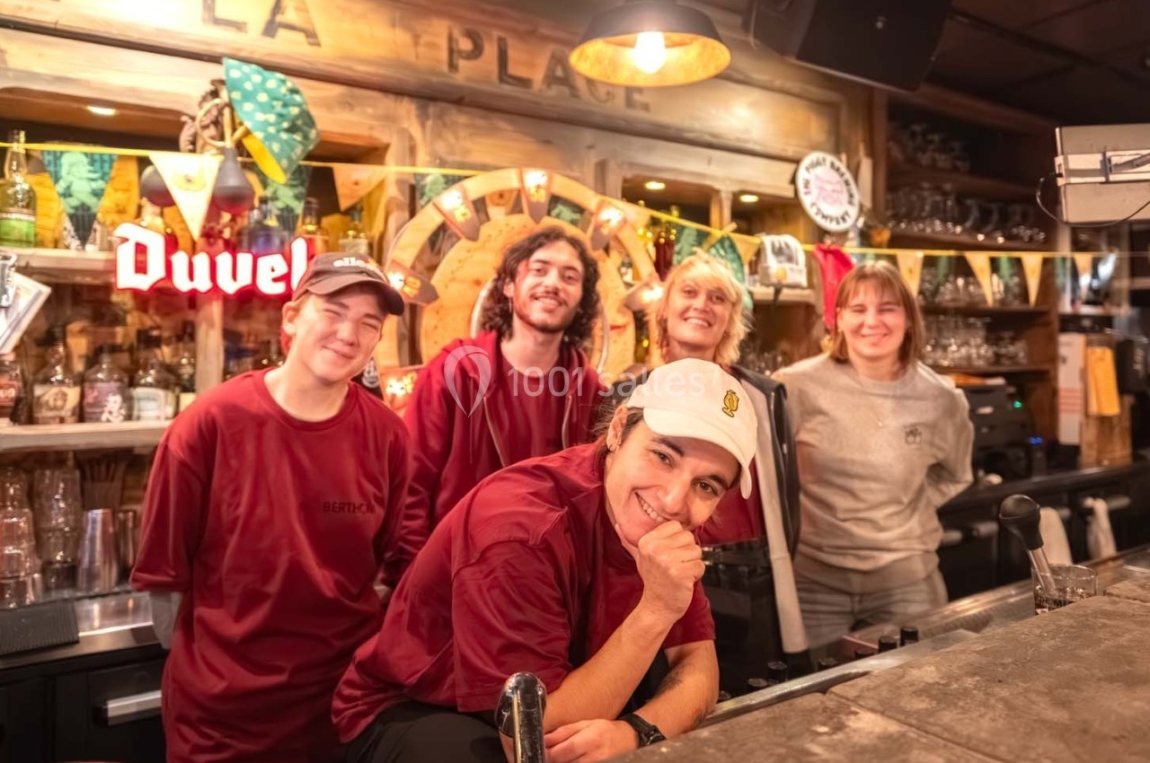 Cinq personnes souriantes posent derrière un comptoir de bar décoré avec des guirlandes et des objets colorés.