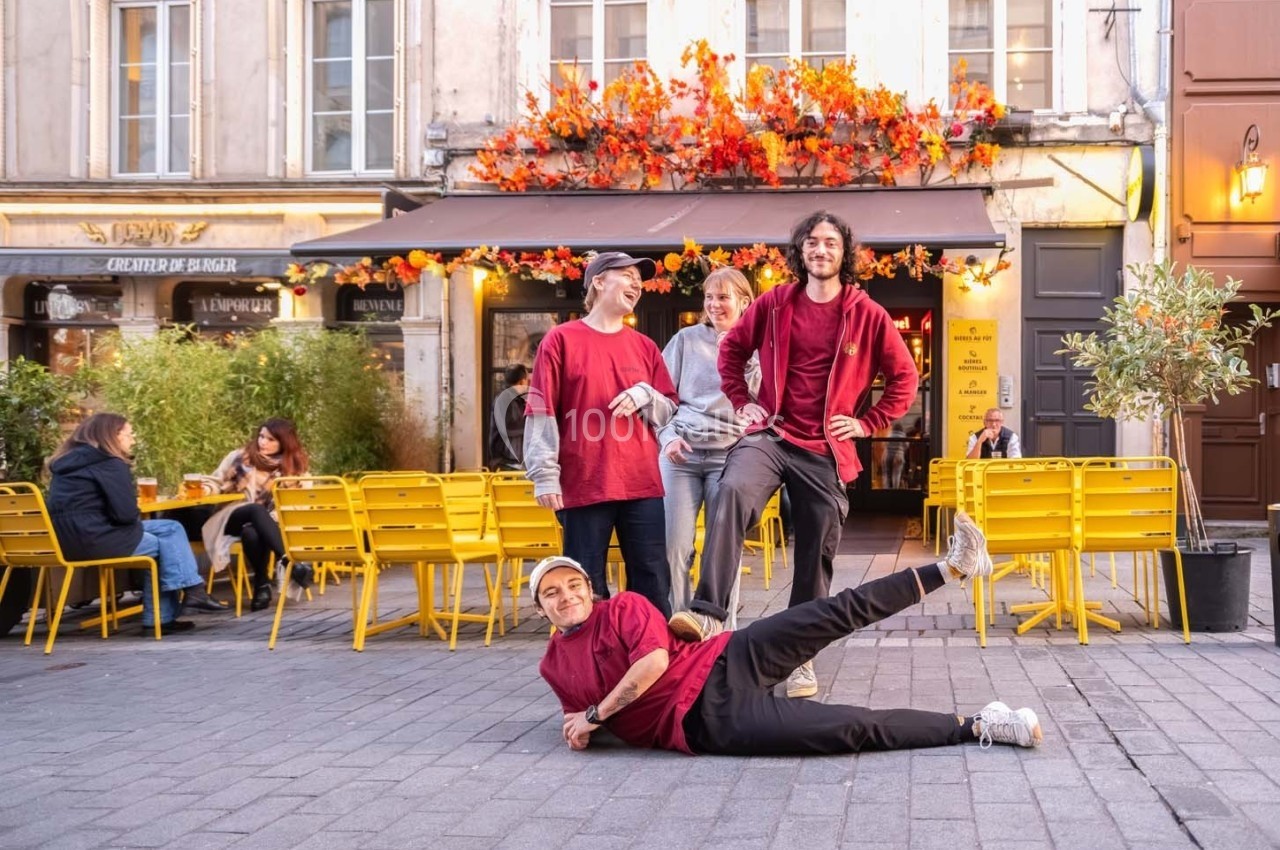 Quatre personnes posent joyeusement devant une terrasse de café décorée de feuillage automnal, avec des chaises jaunes.