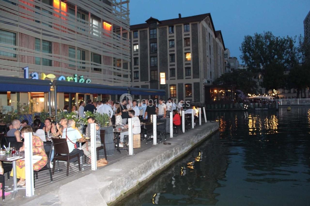 Terrasse bondée d'un restaurant au bord d'un canal, avec des convives profitant de la soirée.