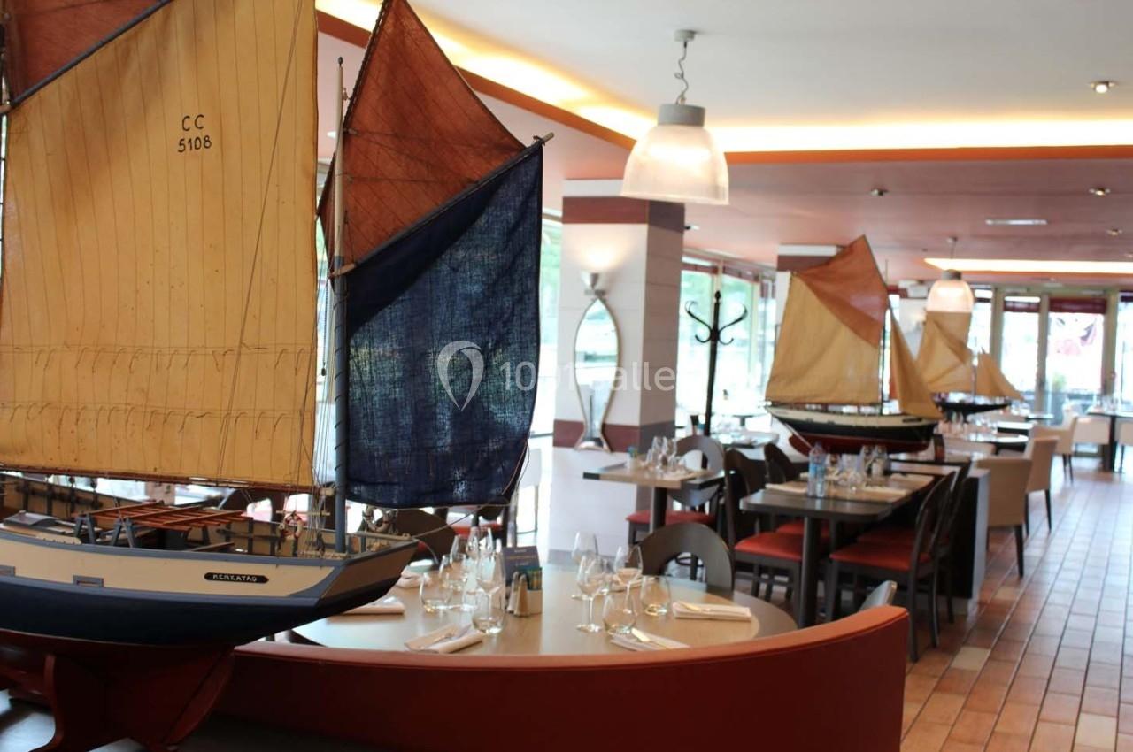 Maquettes de voiliers exposées dans un restaurant lumineux avec tables dressées et décor maritime.