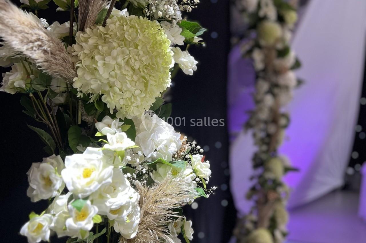 Décoration florale composée de fleurs blanches, d'hortensias et de feuillages, formant une arche élégante.