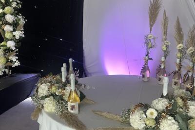 Salle moderne avec tables hautes blanches, éclairage coloré et murs vitrés, prête pour un événement.