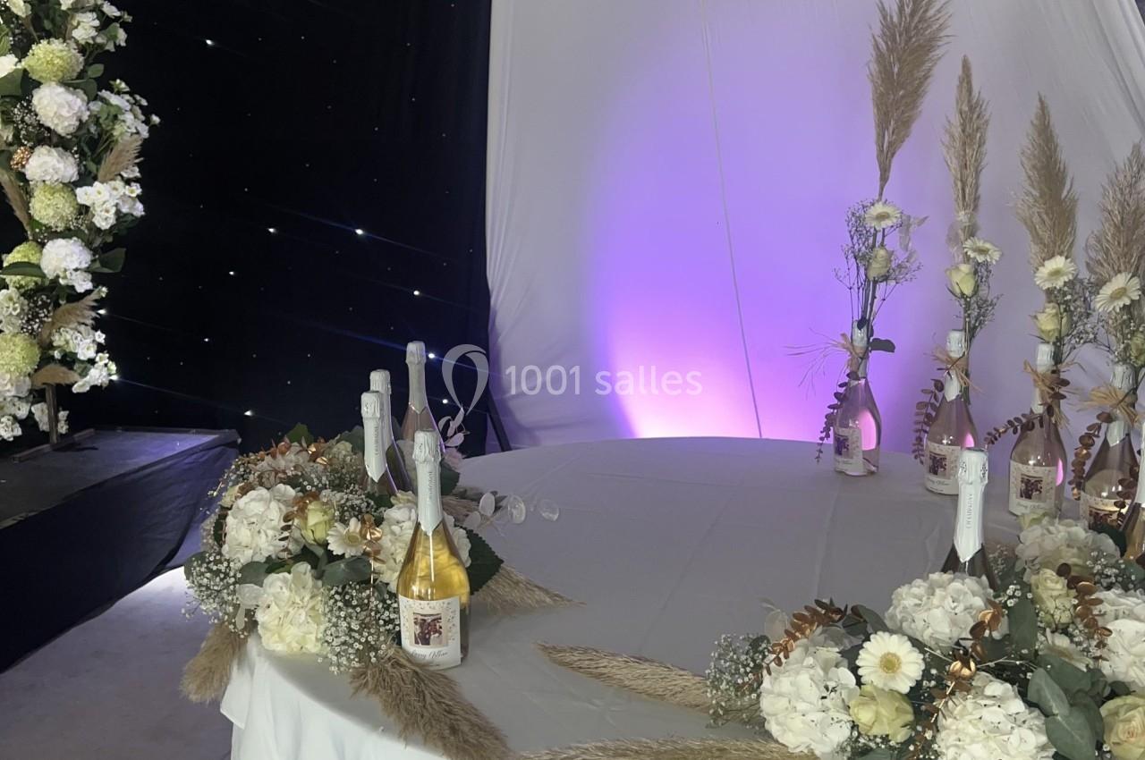 Table décorée avec des fleurs blanches, des pampas et des bouteilles, dans une salle éclairée par des lumières tamisées.