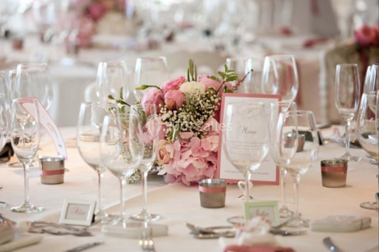 Table élégamment dressée avec des verres, un menu et un centre de table floral composé de roses et d'hortensias.
