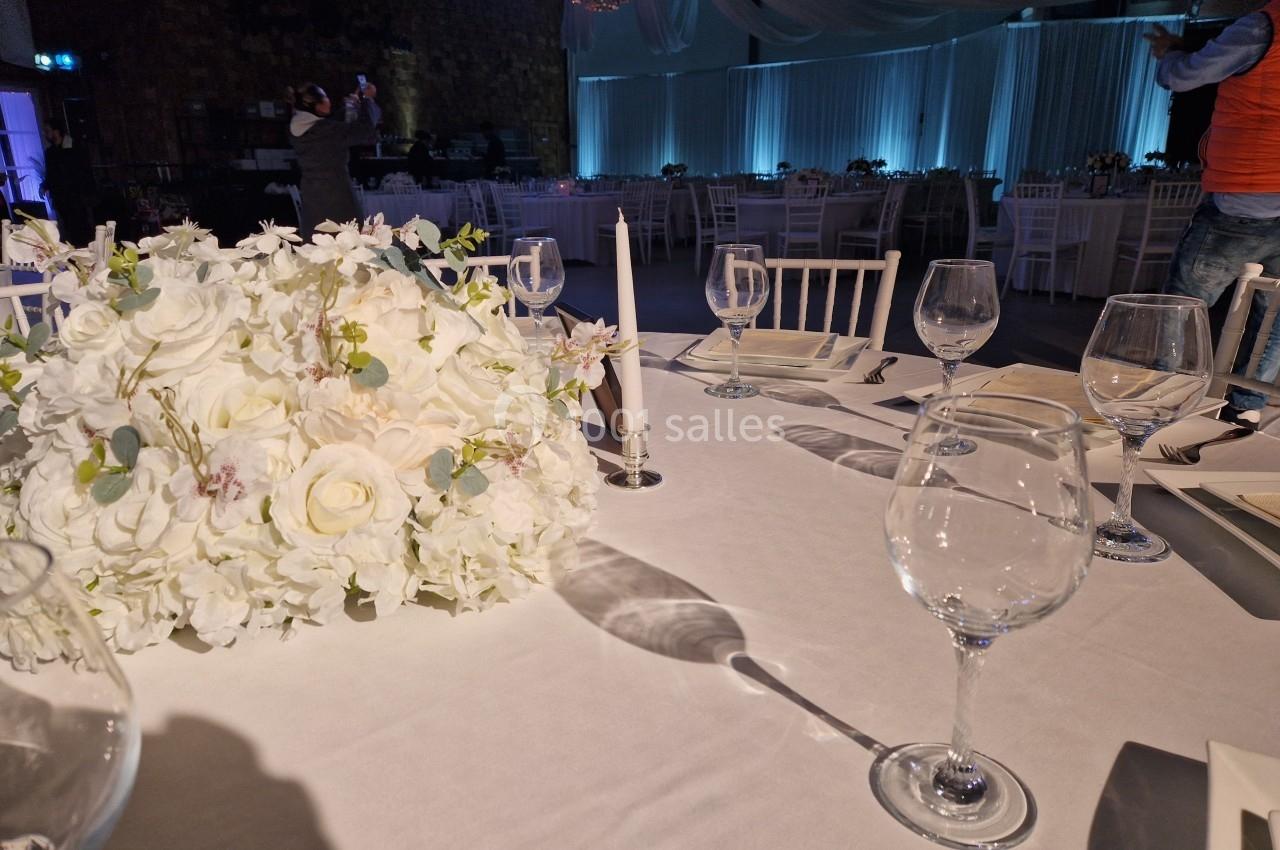Table élégamment dressée avec des verres, des bougies et un centre de table floral blanc dans une salle de réception.