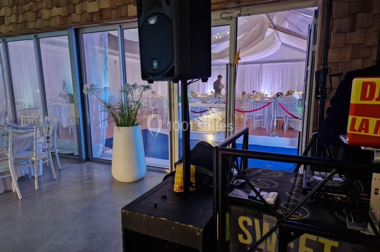 Vue d'une salle de réception décorée avec des tables dressées, prise depuis une zone avec du matériel de sonorisation.